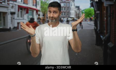 L'homme haussa les deux mains avec des paumes visibles sur une rue pavée à l'extérieur des magasins, face à la caméra avec une expression perplexe ; question d'incertitude. Banque D'Images
