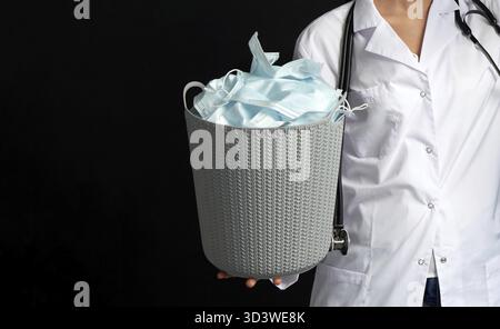 Docteur tenant seau plein de masques faciaux usagés, concept de lutte contre les virus avec poubelle Banque D'Images