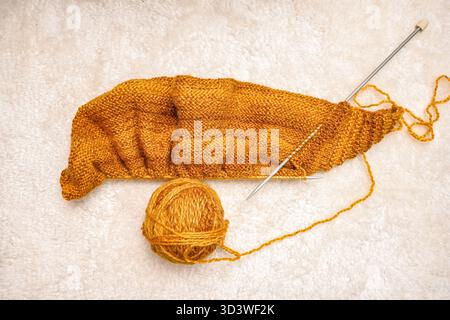 Projet de tricot non fini montrant la boule de fil, les aiguilles et le tissu tricoté sur un fond flou. Banque D'Images