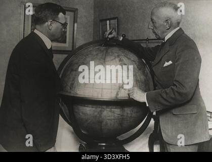 Roald Amundsen (à droite) se tient à côté d'un globe, pointant vers le pôle Nord. La photo a été prise peu avant son départ en 1925. Amundsen était un explorateur polaire de premier plan. Banque D'Images