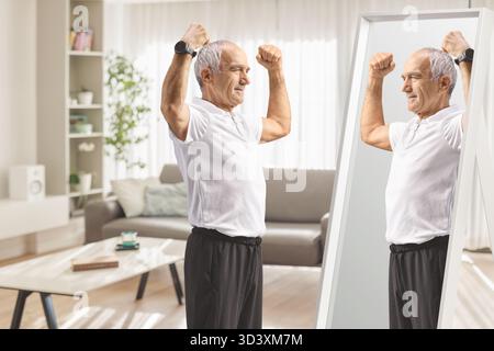 Senior en vêtements de sport fléchissant les muscles du bras devant le miroir à la maison Banque D'Images