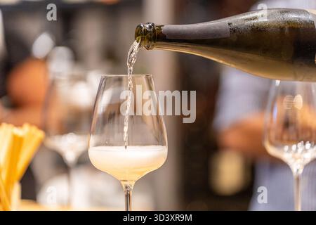 Vin blanc mousseux versé dans un verre de cristal à partir d'une bouteille, créant des bulles Banque D'Images