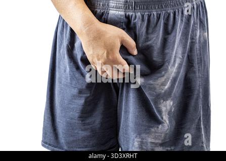 Une personne portant un short foncé se tient debout et tient son entrejambe d'une main, ce qui peut indiquer un malaise. l'image est focalisée sur le bas du corps Banque D'Images