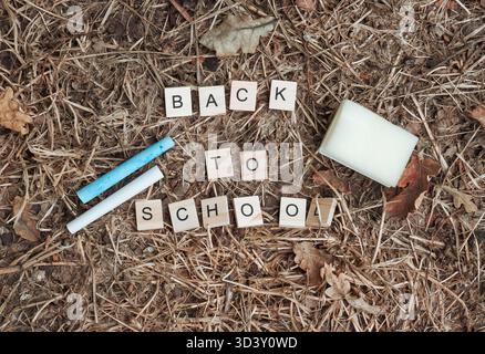 Message de retour à l'école arrangé avec des carreaux de lettres en bois, entouré d'articles de papeterie comme des marqueurs et un bloc d'adhésif, placé sur un na texturé Banque D'Images