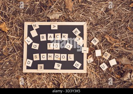 le signe de retour à l'école sur le tableau noir repose dans l'herbe. Concept de début d'année scolaire Banque D'Images