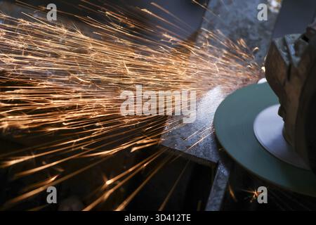 Puissant gros plan de la machine de meulage créant une douche lumineuse d'étincelles chaudes. Travail industriel intense en usine ou en atelier, découpe et polissage méta Banque D'Images