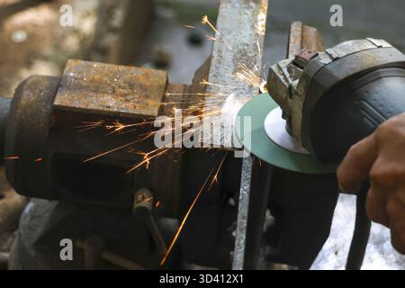 Travailleur concentré broyant le métal avec outil électrique dans l'atelier. Des étincelles chaudes brillantes volent de l'acier pendant que la machine fonctionne, montrant une industria puissante et dangereuse Banque D'Images