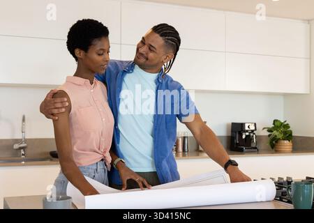 Discuter de couples divers examinant des plans sur l'îlot de cuisine, avec machine à café Banque D'Images