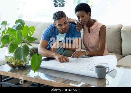 Penchant un couple diversifié étudiant le plan sur une table basse en verre dans le salon, avec tasse Banque D'Images