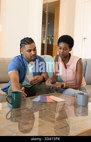 Examen des échantillons de peinture couple divers assis sur le canapé dans le salon moderne, avec des tasses en céramique Banque D'Images