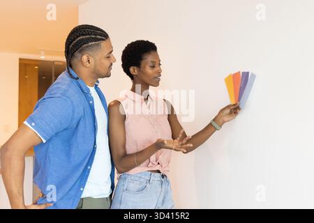 Couple diversifié choisissant des couleurs de peinture dans la chambre à la maison, avec des cartes de nuancier de peinture colorées Banque D'Images