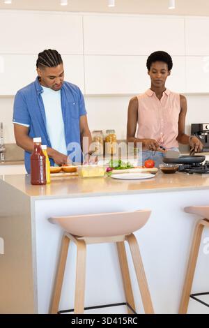 Trancher le pain et remuer la nourriture dans la poêle, cuisiner en couple diversifié à l'îlot de cuisine avec ketchup Banque D'Images