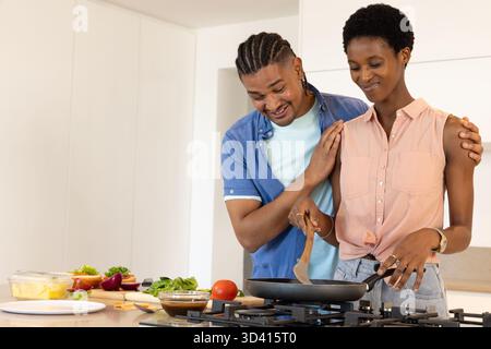 Repas de cuisine de couple diversifié à l'îlot de cuisine maison moderne, avec poêle à frire et légumes frais Banque D'Images