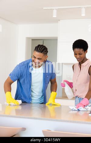 Nettoyage du comptoir d'essuyage de couple diversifié dans la cuisine à domicile, avec flacon pulvérisateur et gants en caoutchouc Banque D'Images