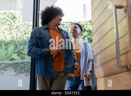 Entrer divers amis masculins entrant dans le hall d'entrée, avec smartphone et tasse à café Banque D'Images