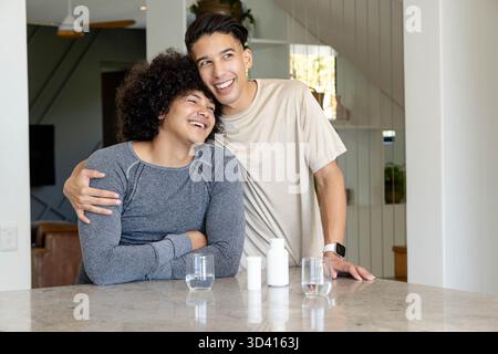 Embrasser divers partenaires masculins s'appuyant sur l'îlot de cuisine, avec des verres et des bouteilles de pilules Banque D'Images