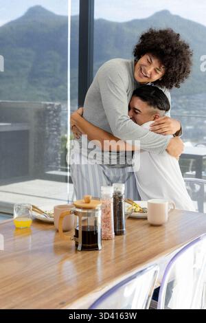 Embrasser divers partenaires masculins debout près de la table de petit déjeuner en bois dans la salle à manger, avec presse française Banque D'Images