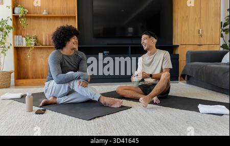 Discuter divers amis masculins assis sur des tapis de yoga dans le salon, avec des bouteilles d'eau et une serviette Banque D'Images