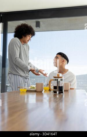 Faire des gestes entre amis masculins partageant le petit déjeuner dans la salle à manger, avec cafetière à presse française Banque D'Images