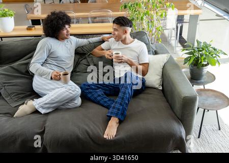 Chatter divers couples masculins assis sur le canapé dans le salon moderne, avec des tasses à café et des plantes Banque D'Images
