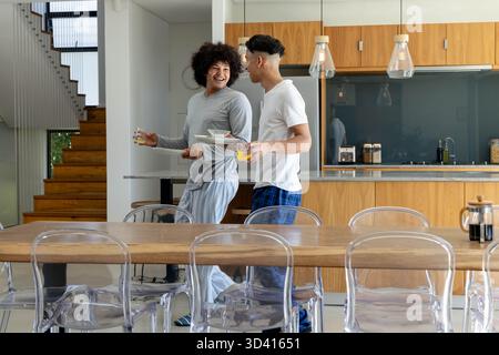 Divers amis masculins portant des assiettes et des verres de petit déjeuner dans une cuisine moderne, avec table à manger Banque D'Images
