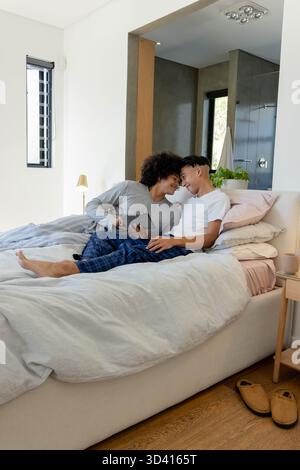 Penchant divers couples masculins touchant les fronts sur le lit dans une chambre moderne, tenant la tablette Banque D'Images