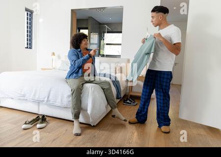 Pointant et souriant, divers amis masculins sélectionnant chemise verte sur cintre dans la chambre Banque D'Images