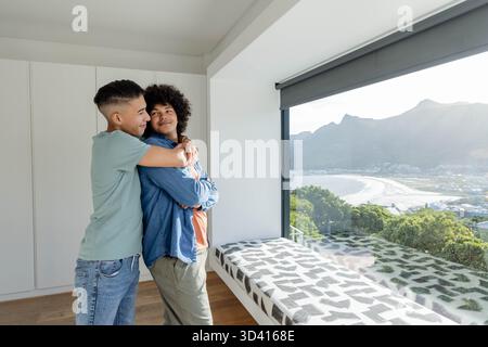 Embrasser divers partenaires masculins debout dans la maison côtière moderne avec fenêtre panoramique, espace de copie Banque D'Images