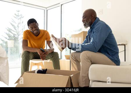 Déballage père afro-américain et fils ouvrant des boîtes dans le salon avec chaussure et smartphone Banque D'Images
