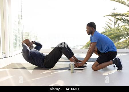 Client afro-américain faisant des sit-ups avec entraîneur dans le studio de fitness, avec tapis et bouteille d'eau Banque D'Images