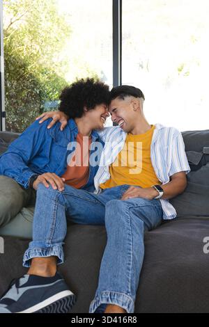 Rire deux hommes penchés les têtes ensemble sur le canapé dans le salon, avec une grande fenêtre et smartwatch Banque D'Images