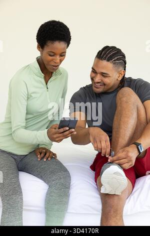 Montrant divers amis assis sur le lit dans la chambre, avec smartphone, smartwatch et baskets blanches Banque D'Images