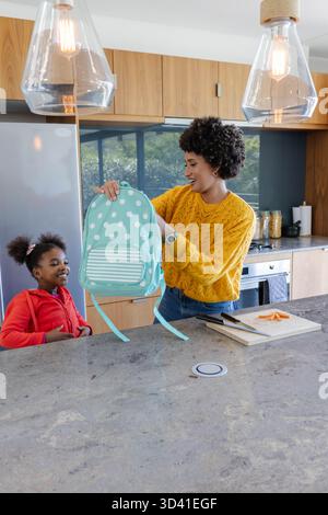 Mère et fille afro-américaine examinant le sac à dos à pois au comptoir de granit, avec des pots Banque D'Images