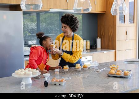 Nourrir une mère et une fille variées en dégustant un cupcake givré sur l'île de marbre, avec des outils de cuisson Banque D'Images