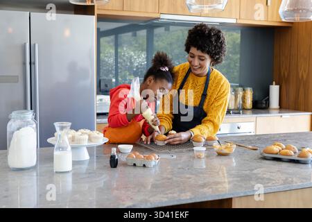 Décoration diversifiée mère et fille glaçage de cupcakes sur le comptoir de l'îlot de cuisine en marbre Banque D'Images