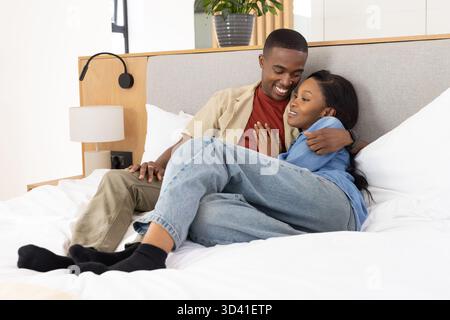 Se prélasser couple afro-américain embrassant doucement sur un lit blanc dans une chambre moderne, avec lampe en céramique Banque D'Images