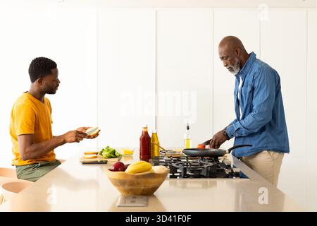 Cuisine afro-américaine père et fils préparant le petit déjeuner à l'îlot de cuisine, avec plaque de cuisson à gaz Banque D'Images