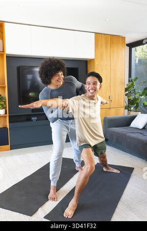 Professeur de yoga masculin et étudiant pratiquant la pose large dans un salon moderne, avec des tapis de yoga Banque D'Images