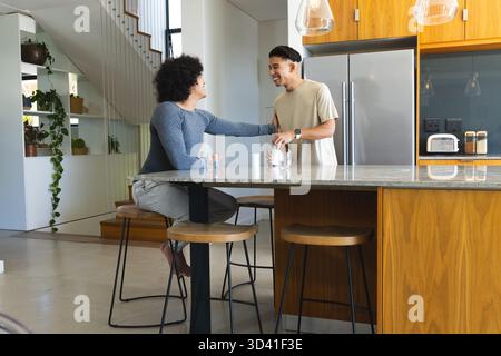 Bavarder divers amis masculins se penchant sur l'îlot de cuisine dans la cuisine moderne, avec des verres à boire Banque D'Images
