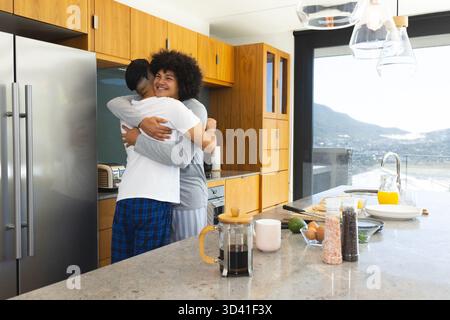 Embrassant divers partenaires masculins debout dans une cuisine lumineuse près des portes, avec presse française, espace de copie Banque D'Images