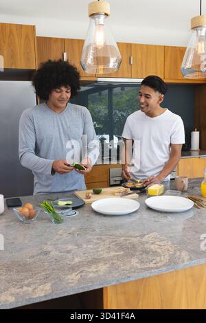 Hacher l'avocat et assembler des toasts par divers amis masculins dans la cuisine à la maison, avec des herbes fraîches Banque D'Images