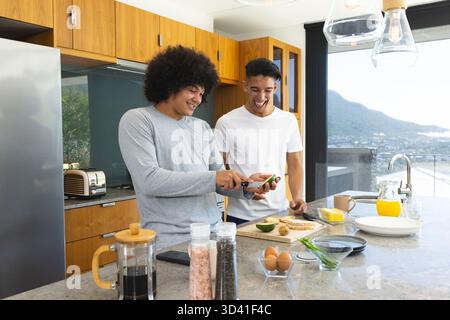 Hacher l'avocat sur la planche à découper, divers amis masculins préparant le petit déjeuner dans la cuisine moderne Banque D'Images