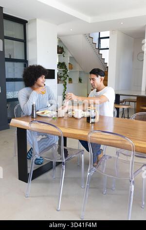 Assis divers amis masculins partageant le petit déjeuner à la cuisine à la maison, avec presse française et jus d'orange Banque D'Images