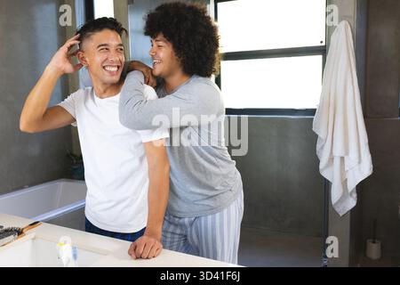 Embrasser divers partenaires masculins souriant à l'évier de salle de bains moderne, avec brosse à dents et brosse à cheveux Banque D'Images