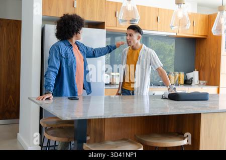 Discuter divers amis masculins à l'îlot de cuisine dans la cuisine moderne, avec smartphone et mallette Banque D'Images