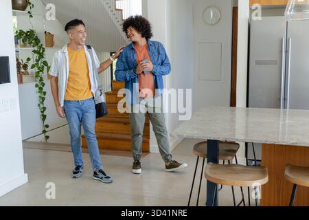 Divers amis masculins marchant à travers le foyer moderne portant un sac à bandoulière, passant l'île avec des tabourets Banque D'Images