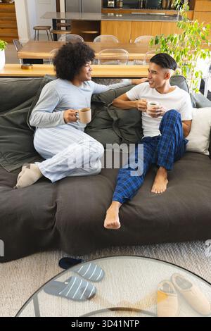 Chatter divers couples masculins sirotant un café sur un canapé vert foncé dans le salon, avec des tasses en céramique Banque D'Images