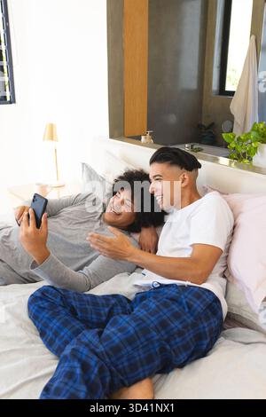 Discuter divers amis masculins assis sur le lit dans une chambre moderne, avec smartphone et oreillers Banque D'Images