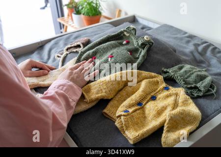 Femme enceinte choisissant des vêtements pour bébé à la maison, attendant la mère se préparant pour le nouveau-né et choisissant une tenue pour bébé avec amour et anticipation Banque D'Images