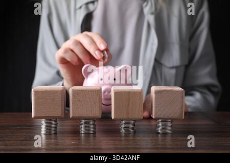 Femme mettant la pièce dans la tirelire à la table en bois, se concentrer sur les cubes vierges et l'argent. Maquette pour le design Banque D'Images